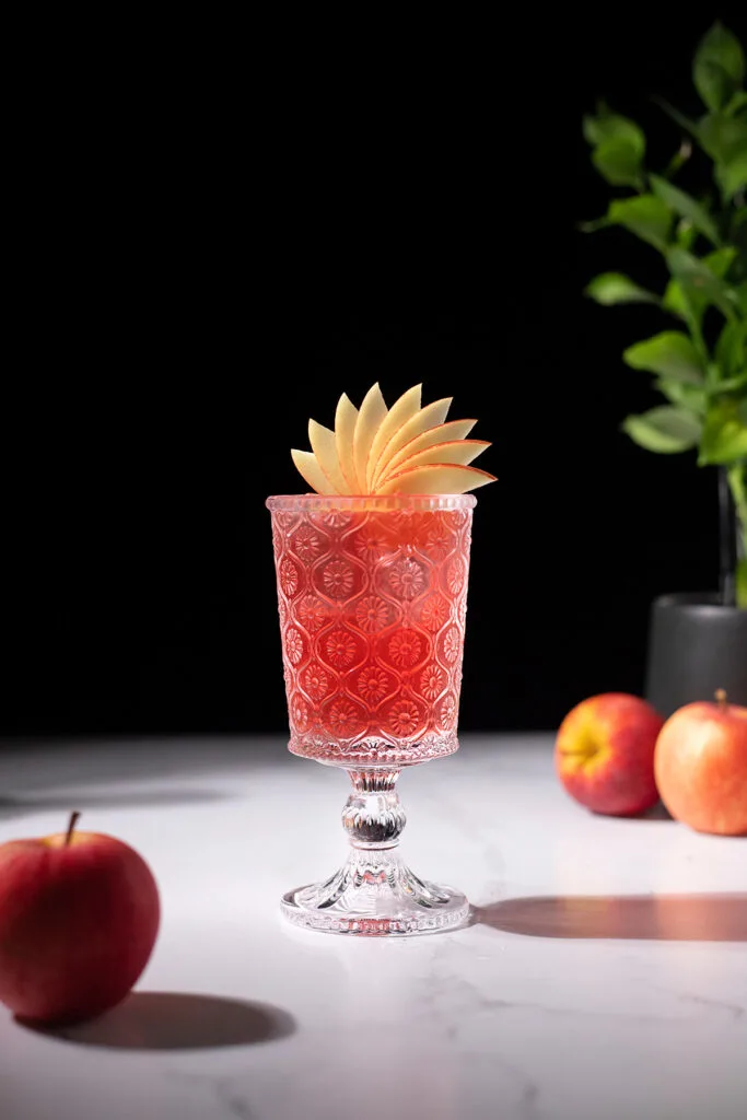 a red drink garnished with a fancy apple fan.