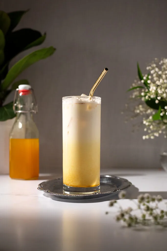 a tall creamy yellow drink with a gold metal straw.