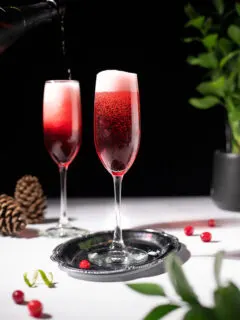 champagne flutes filled with a red cocktail with a frothy head.