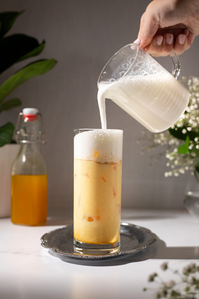 pouring frothed milk into a glass of iced golden milk.