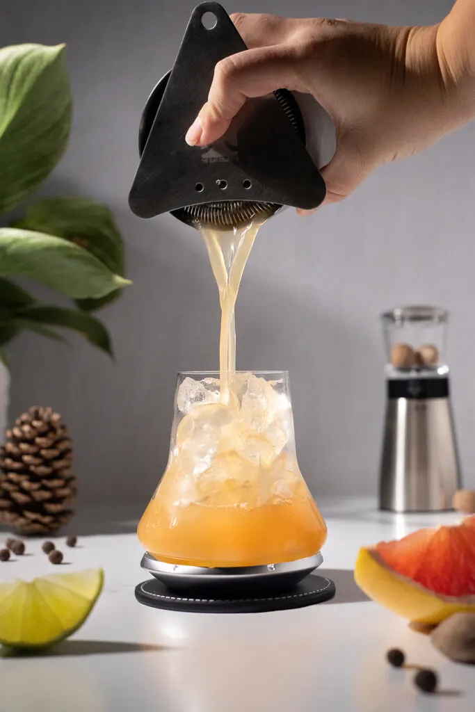 straining the cocktail into a fancy whiskey glass filled with ice.