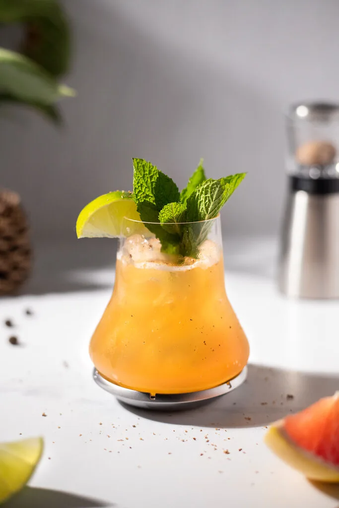 a whiskey and grapefruit cocktail garnished with a lime wedge and mint leaves.