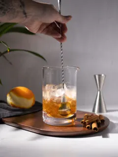 stirring a brown cocktail in an etched mixing glass.