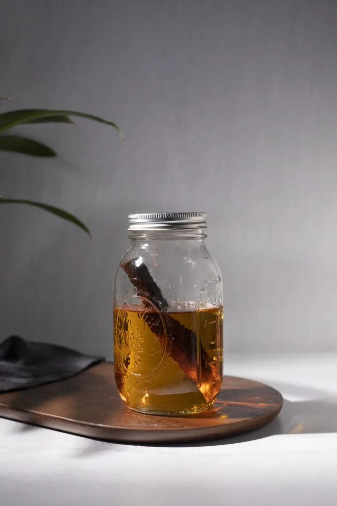 a mason jar filled with brown liquor and a stick of birch wood.