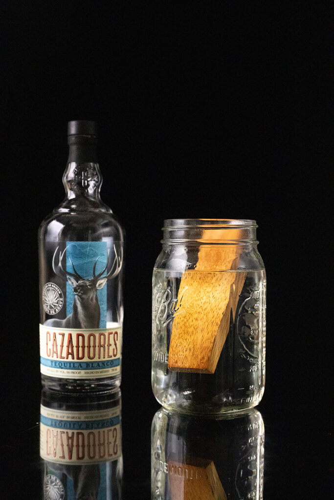 a bottle of Cazadores blanco tequila next to a mason jar filled with tequila and amburana wood.