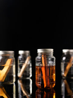 four mason jars filled with different liquors and sticks of wood.