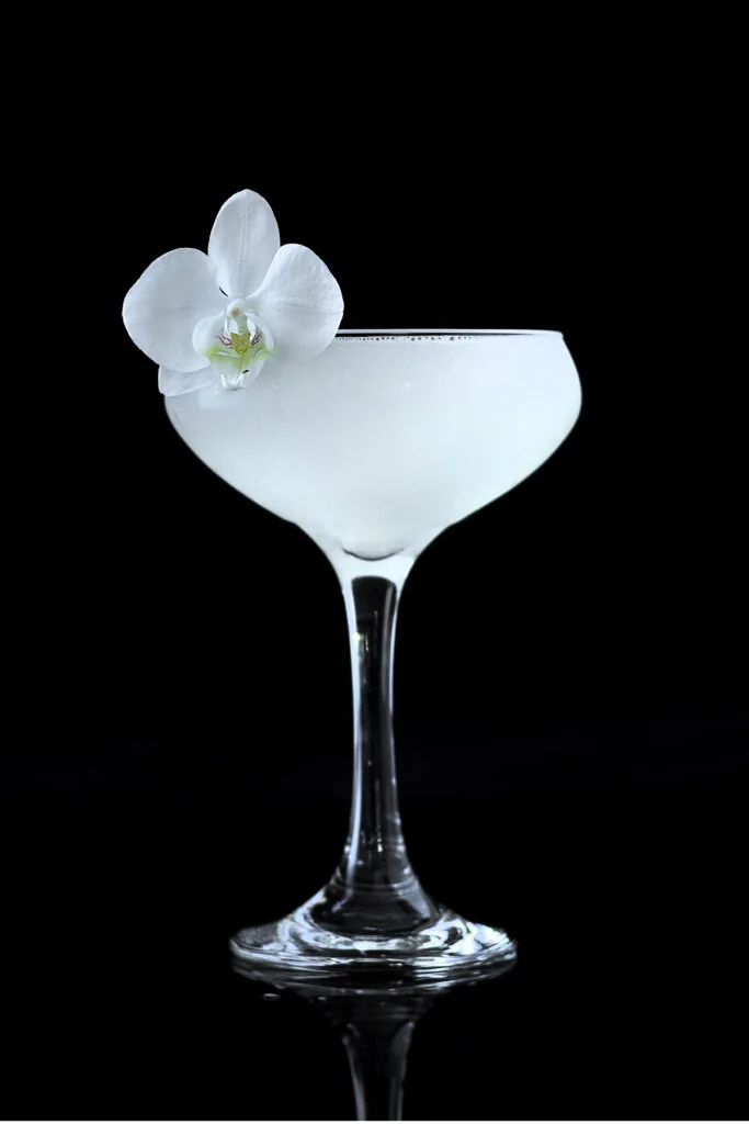 a white cocktail in a coupe glass garnished with a white orchid.