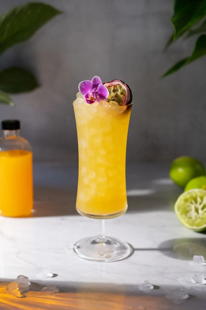 A tall yellow tropical drink in a hurricane glass.