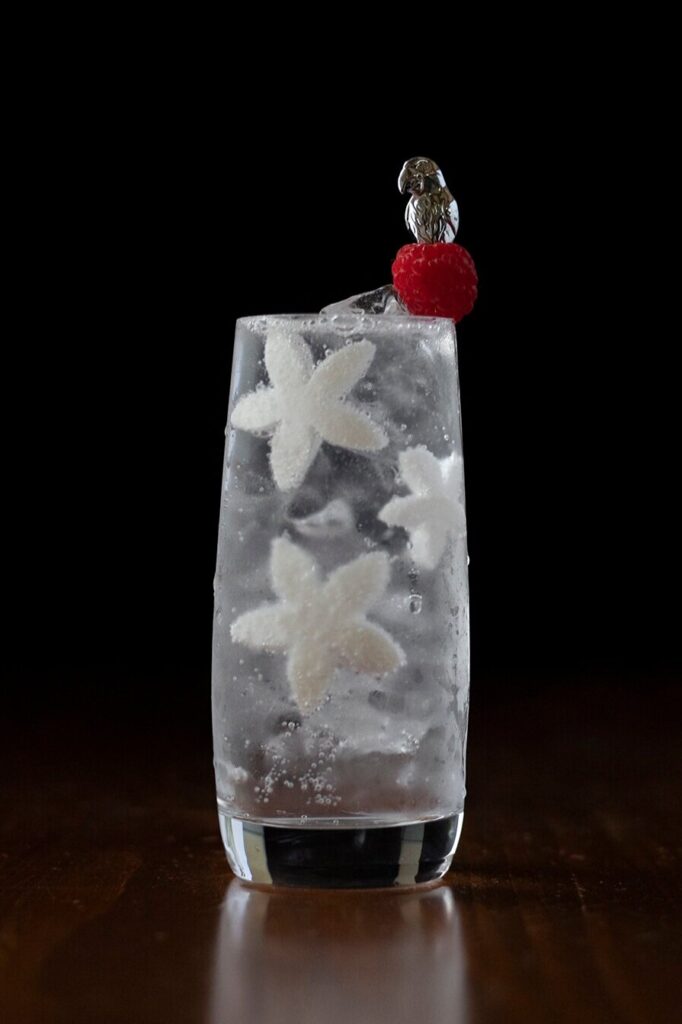 a highball glass filled with clear bubbly liquid and white coconut star cutouts.