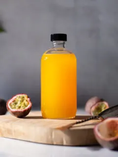a glass bottle of bright yellow syrup next to passion fruits.