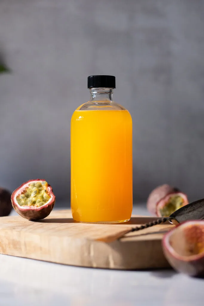 a glass bottle of bright yellow syrup next to passion fruits.