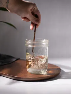 stirring simple syrup with a bronze spoon in a glass jar.