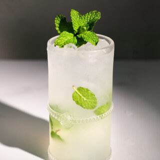 a tall glass filled with a bubbly drink with mint leaves.