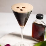 brown cocktail in a martini glass garnished with three coffee beans.