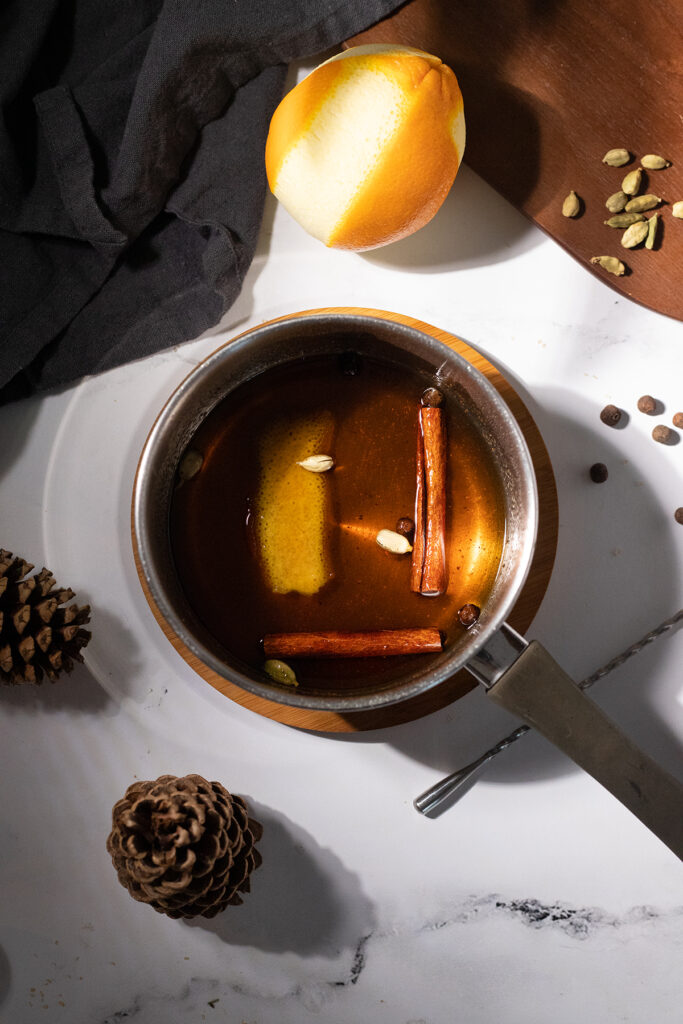 brown liquid with spices and an orange peel in a saucepan.