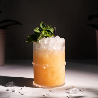 a tan colored cocktail in a rocks glass with crushed ice and mint sprig.