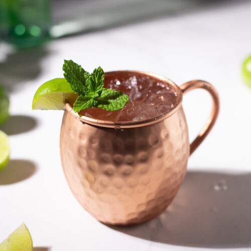copper mule mug filled with icy liquid and garnished with mint sprig and lime wedge.