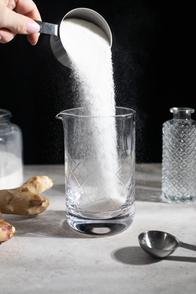 pouring sugar from measuring cup into glass container.
