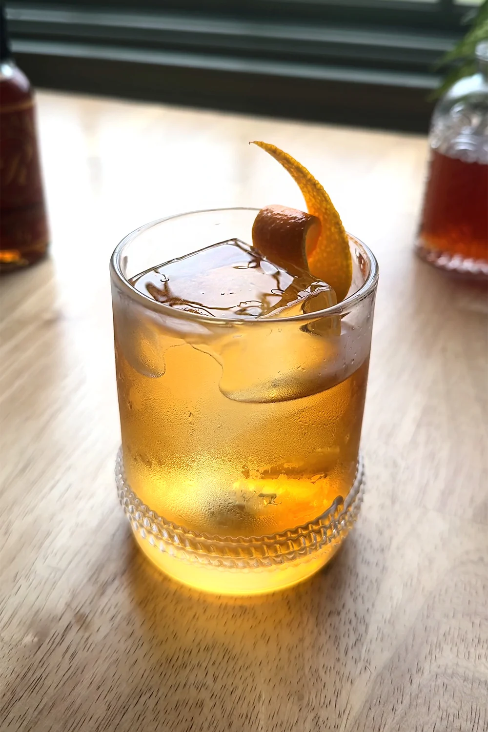 golden colored cocktail in a lowball glass with a curled orange peel garnish.