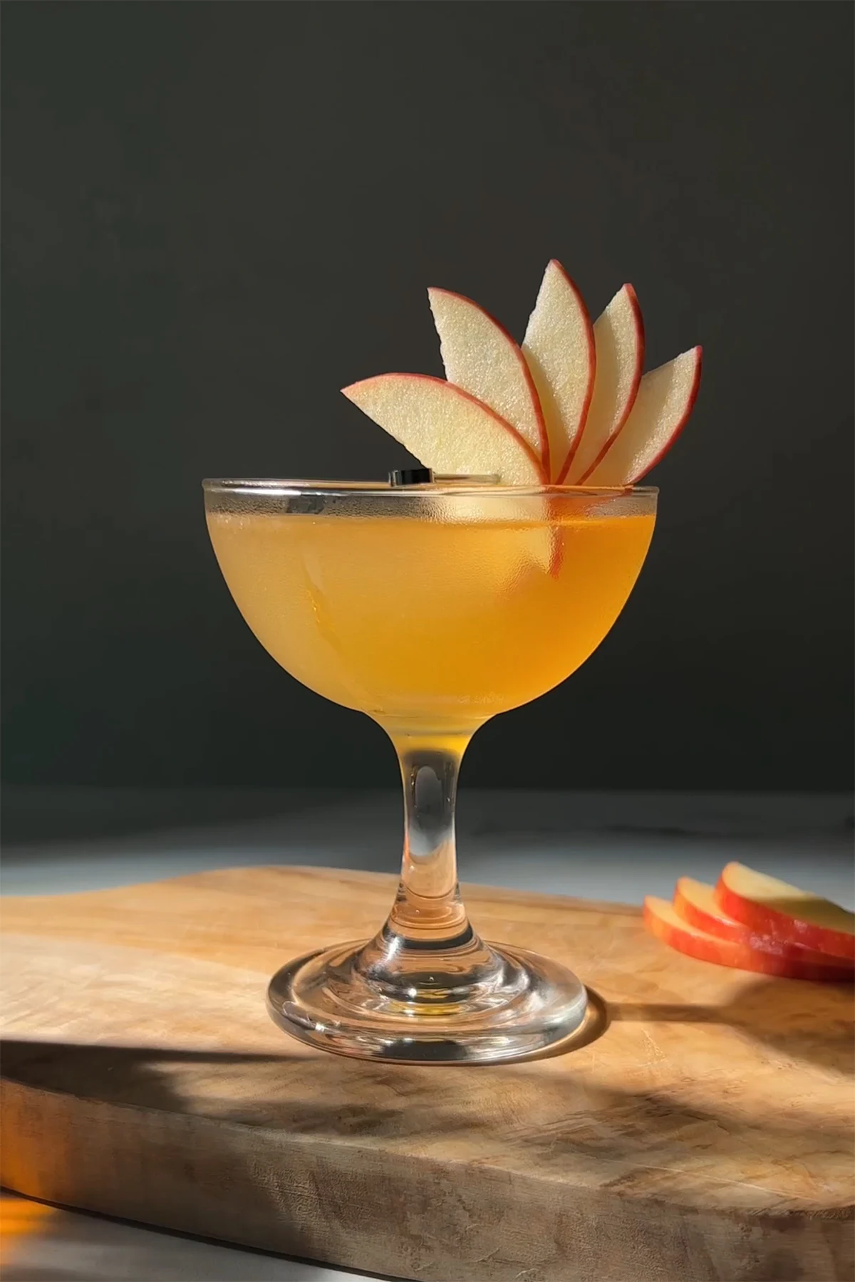 golden colored cocktail in a coupe glass garnished with an apple fan.