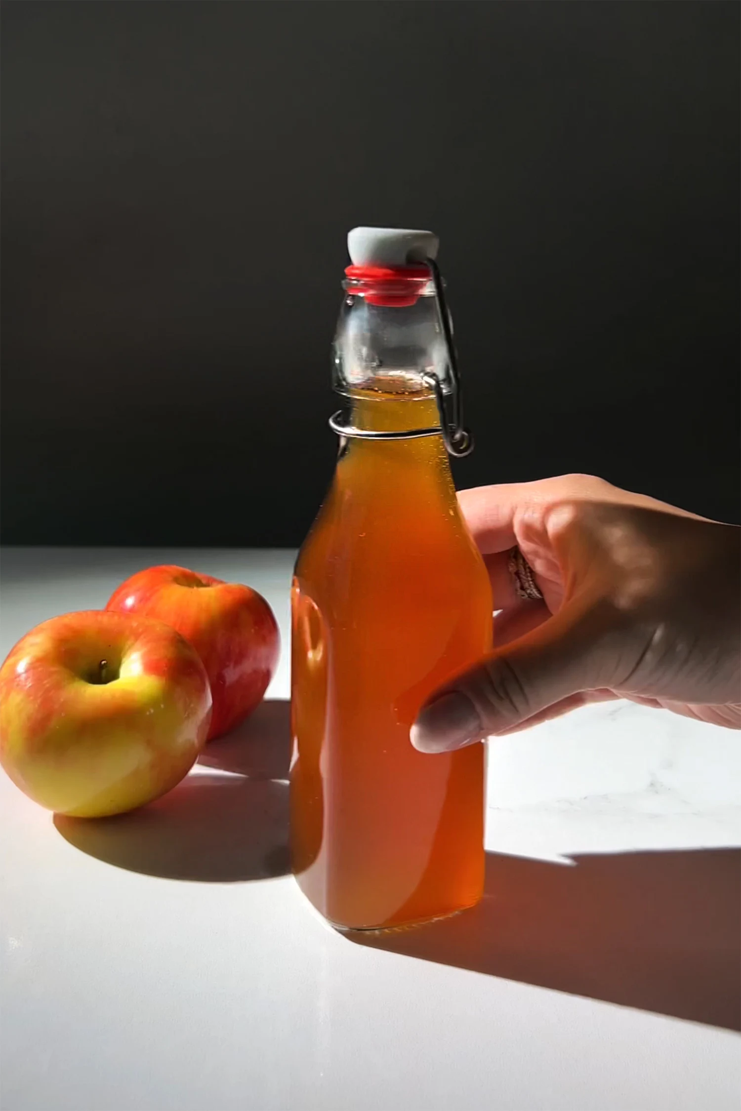 hand holding a glass swing top bottle filled with golden brown syrup.