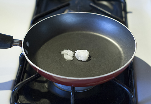 lump of coconut oil in a black nonstick frying pan.