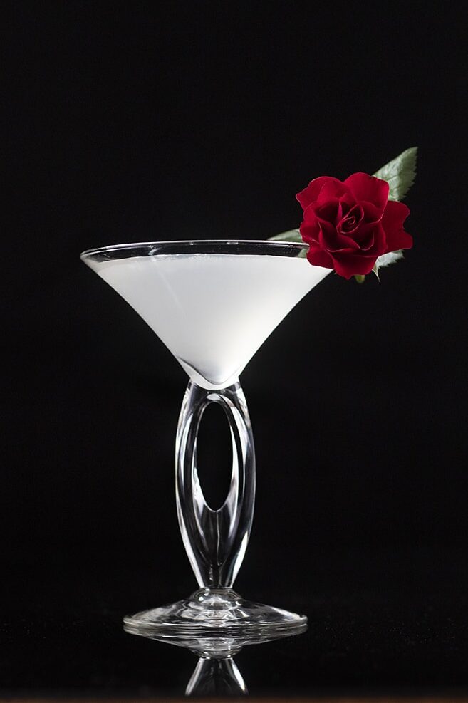 white liquid in a martini glass with a red rose on the rim.