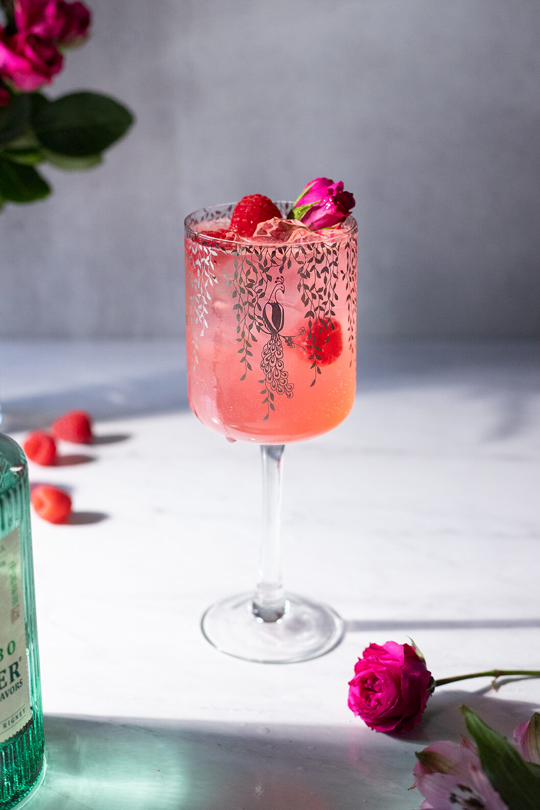 a tall wine glass filled with a pink drink with raspberries and a rose.