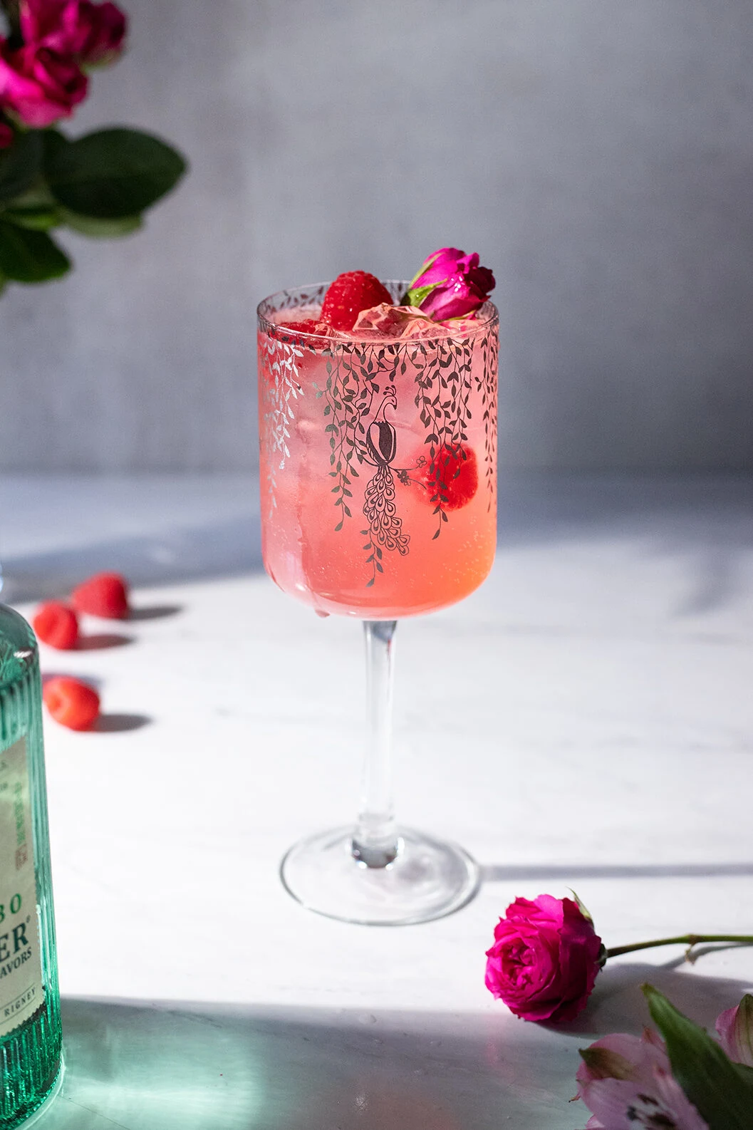 a tall wine glass filled with a pink drink with raspberries and a rose.